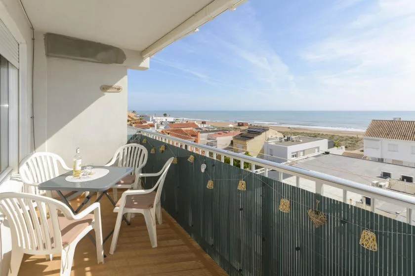 A balcony with outdoor seating overlooks nearby buildings and the sea.
