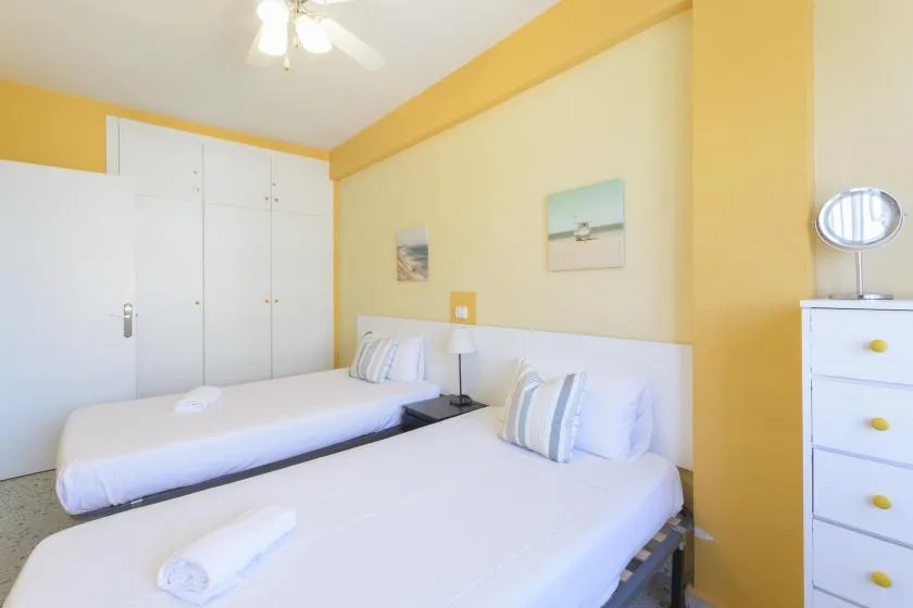 A bright bedroom with two beds, white linens, and yellow walls.