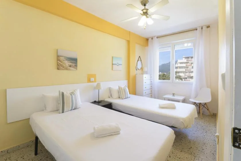 A bright bedroom with two beds, a window, and a ceiling fan.