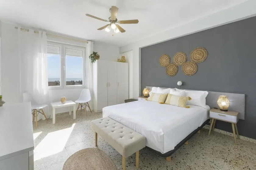 A bright bedroom with a white bed, a bench, and windows.