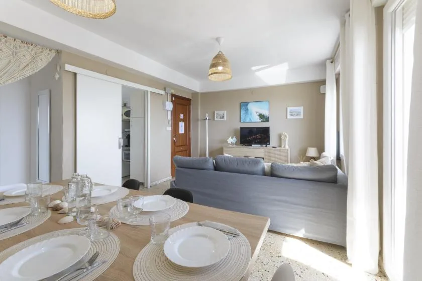 A dining area opens onto a living room with a television and large windows.
