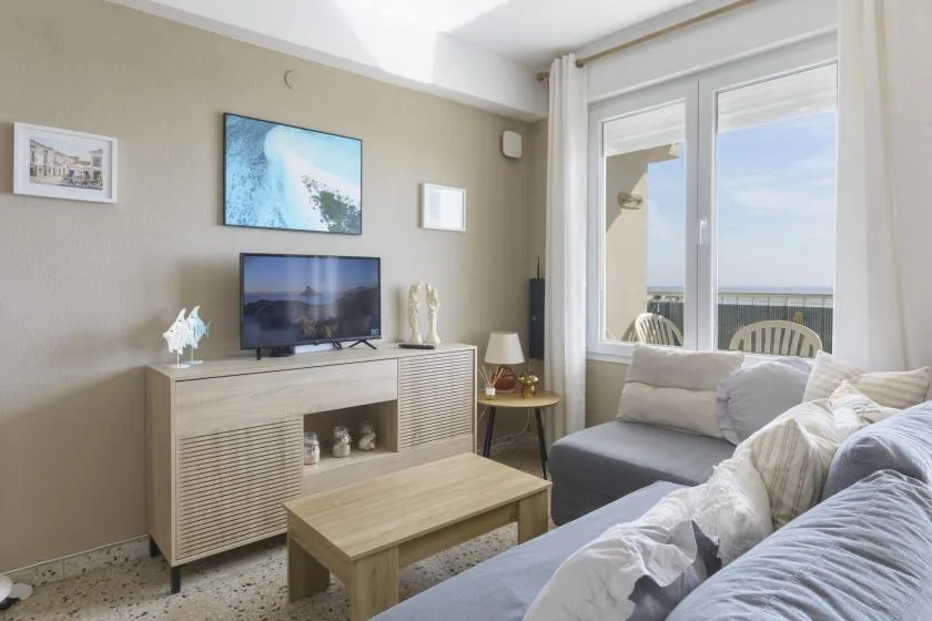 A bright living room with a television, seating, and glass doors opening onto a balcony.