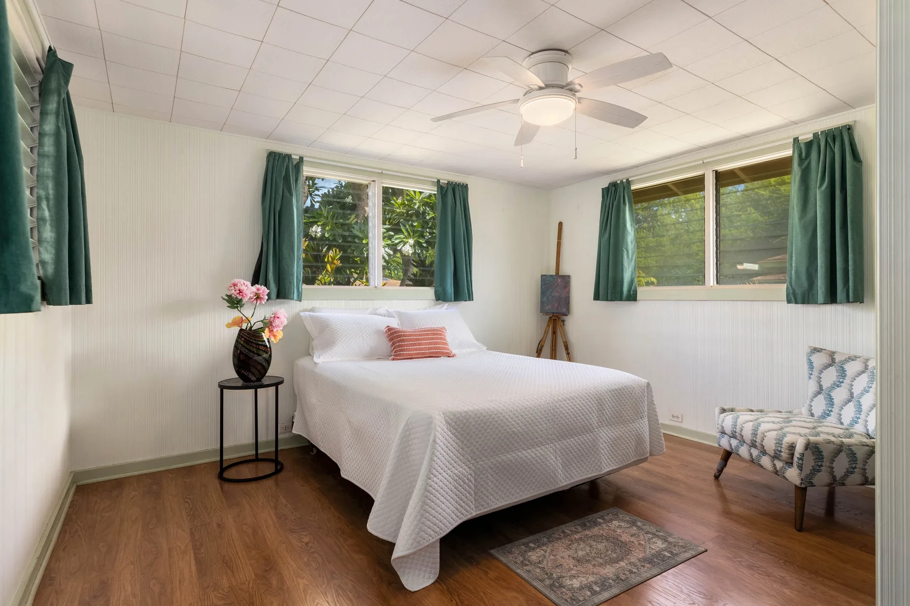 A bedroom with a white bed, green curtains, and a ceiling fan.