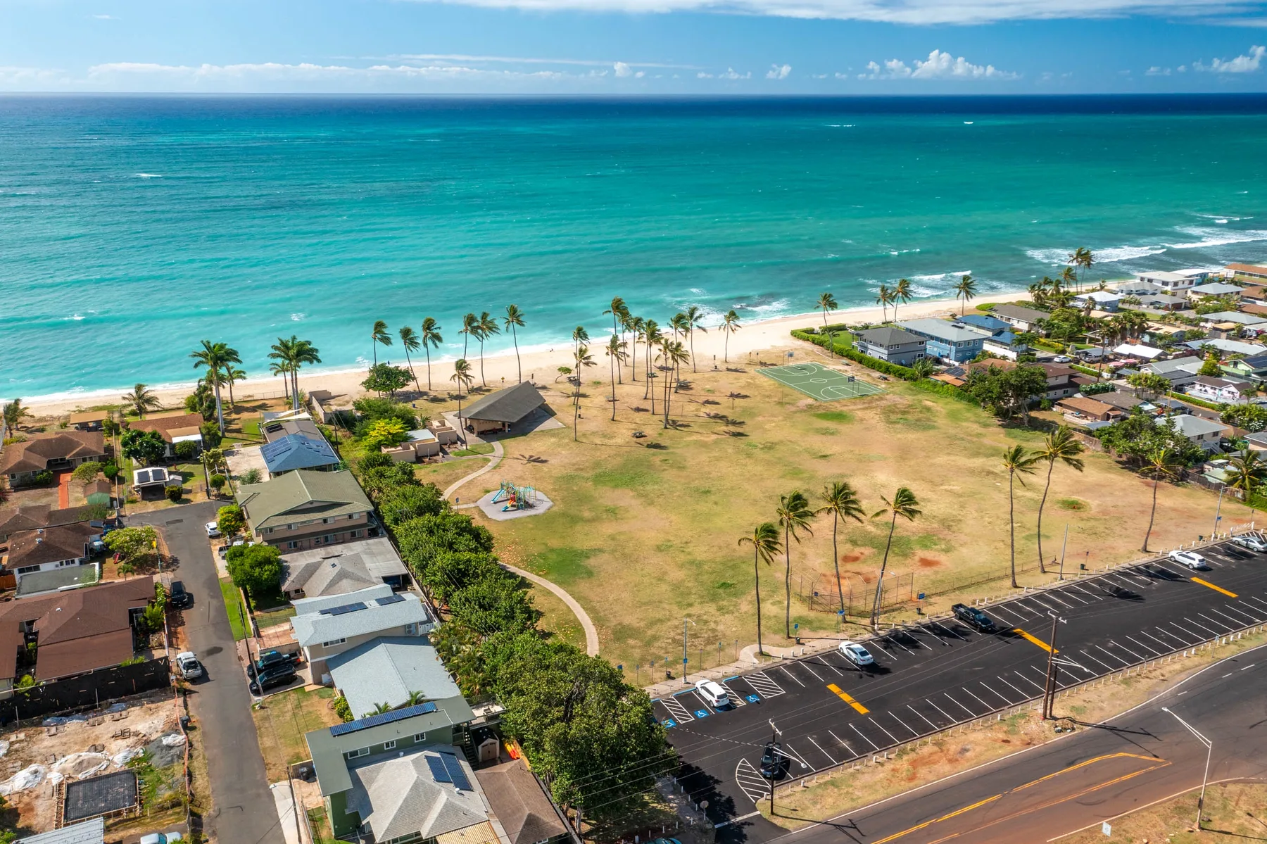 An aerial view shows a coastal neighborhood beside a broad beach and turquoise ocean.