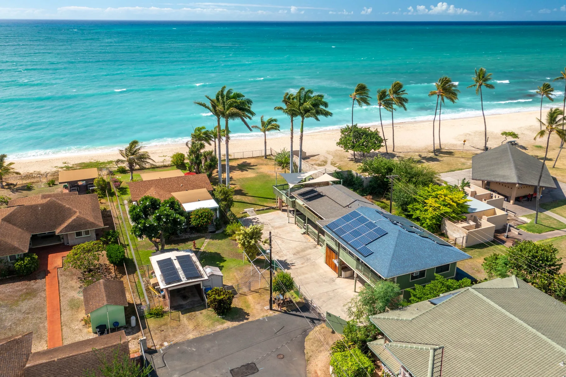 Aerial view of beachfront buildings with palm trees along a sandy shore.