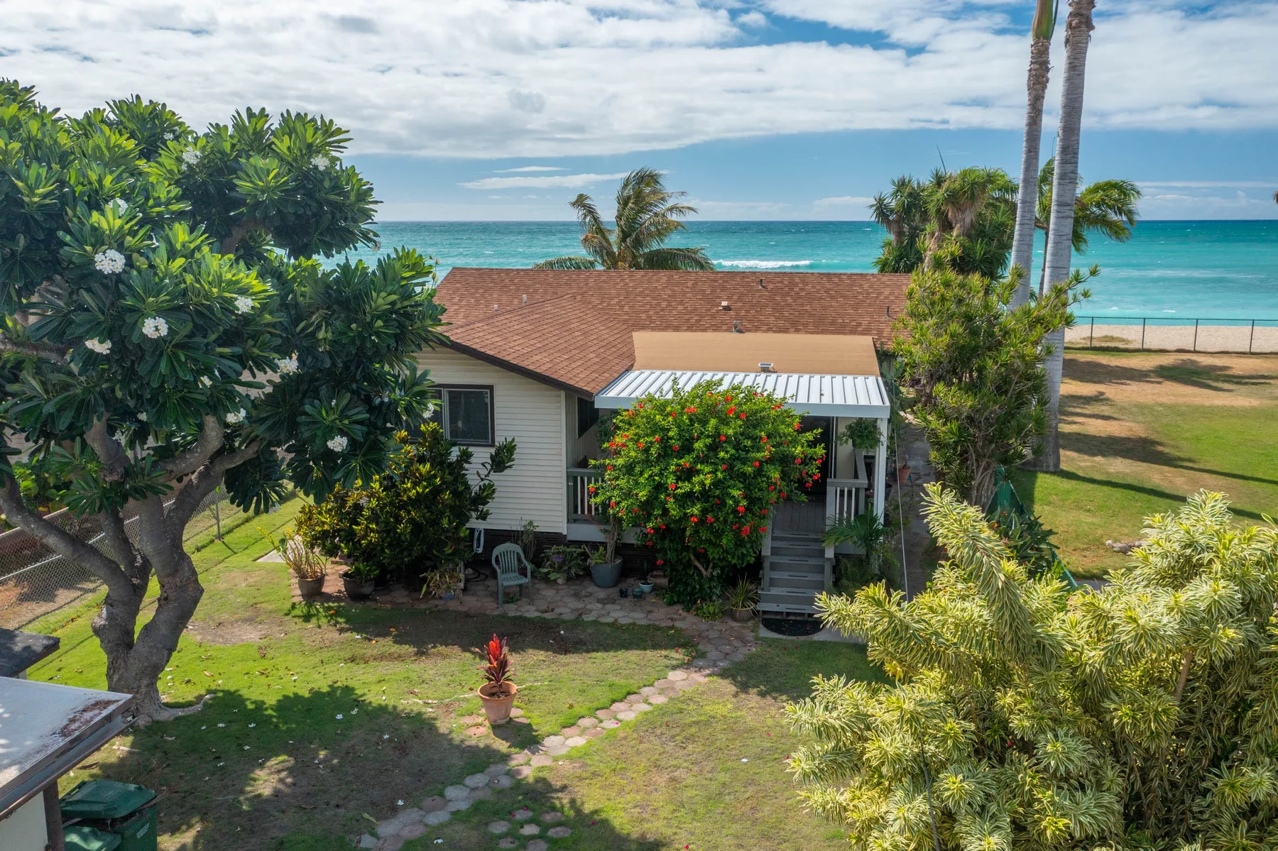 A small house with a garden sits beside the turquoise sea under a cloudy sky.