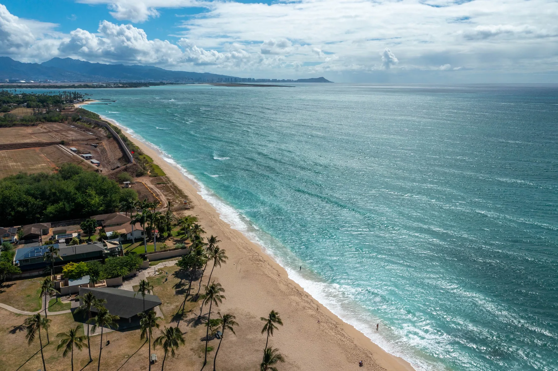 Aerial view of a sandy coastline with turquoise ocean water and palm trees.