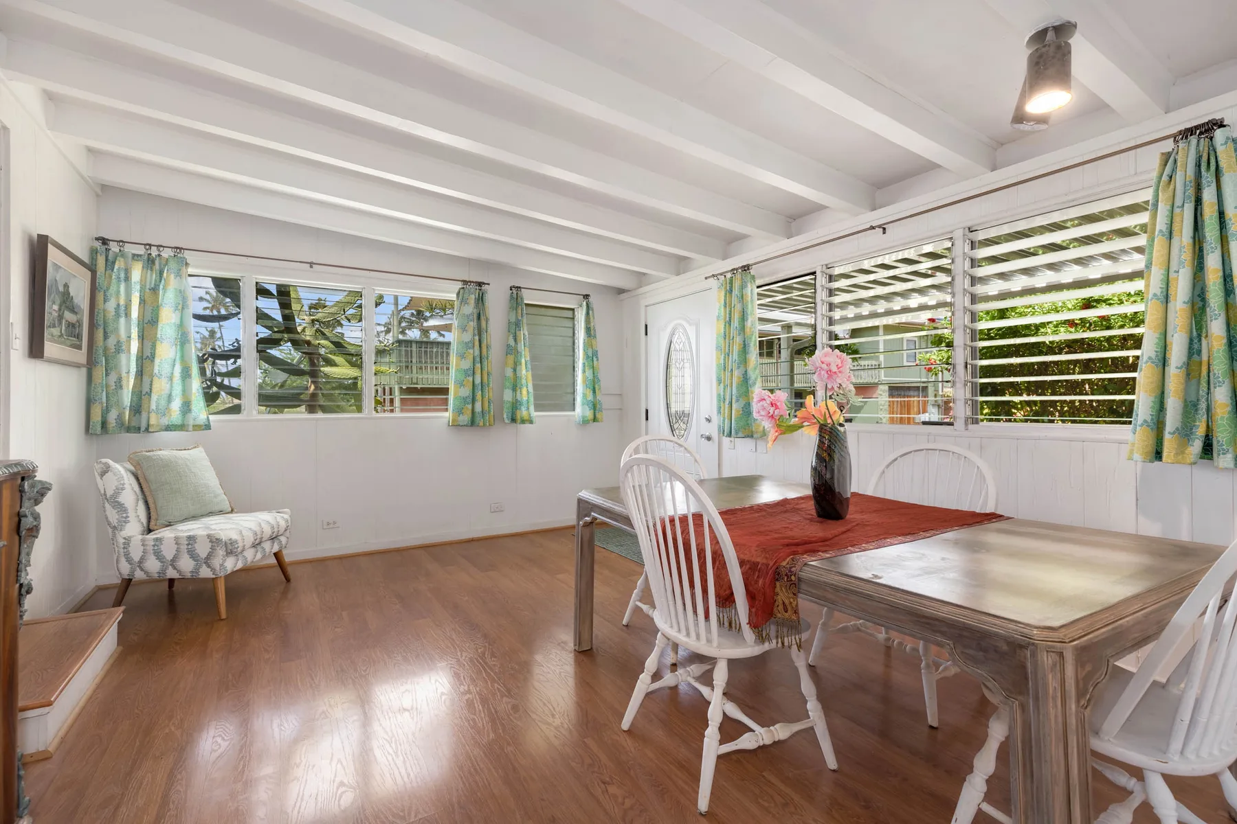 A bright dining area with a wooden table, white chairs, and large windows.