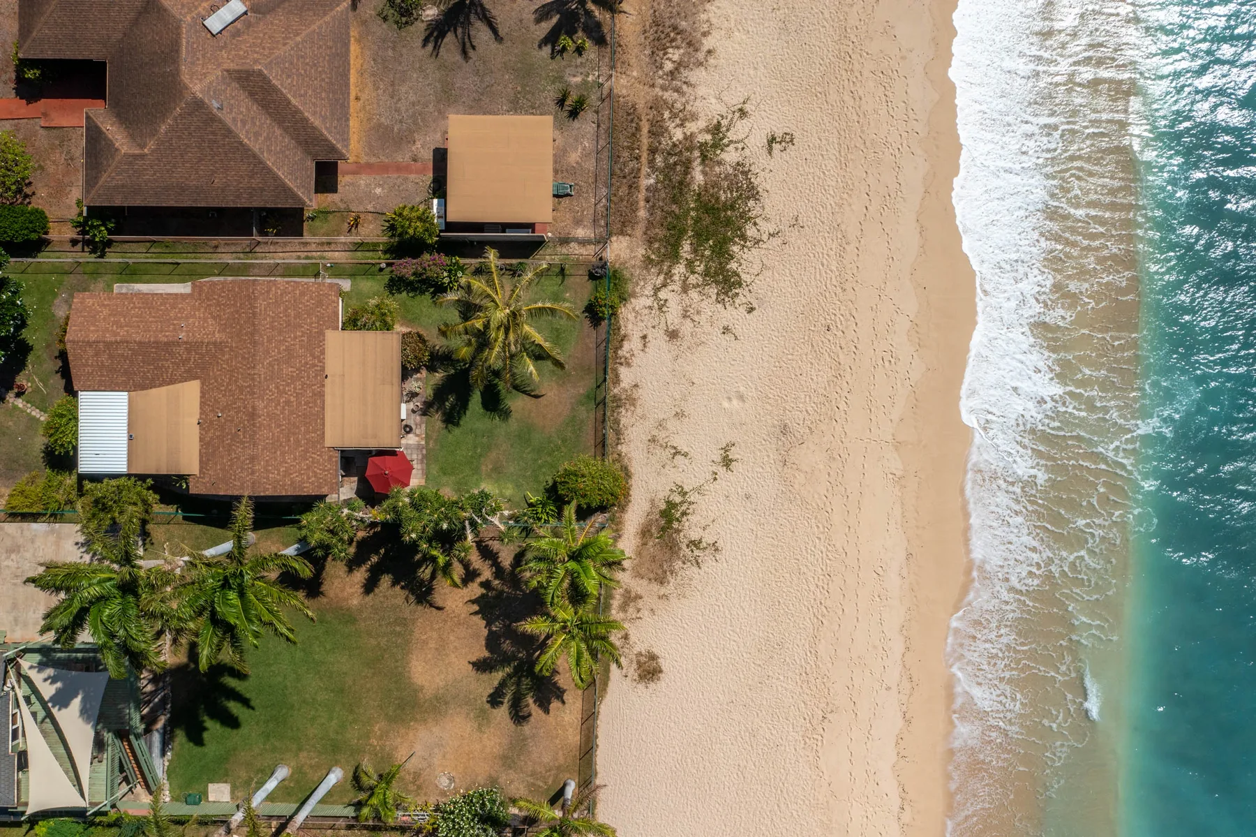 An aerial view shows beachfront buildings beside a sandy shore and breaking waves.
