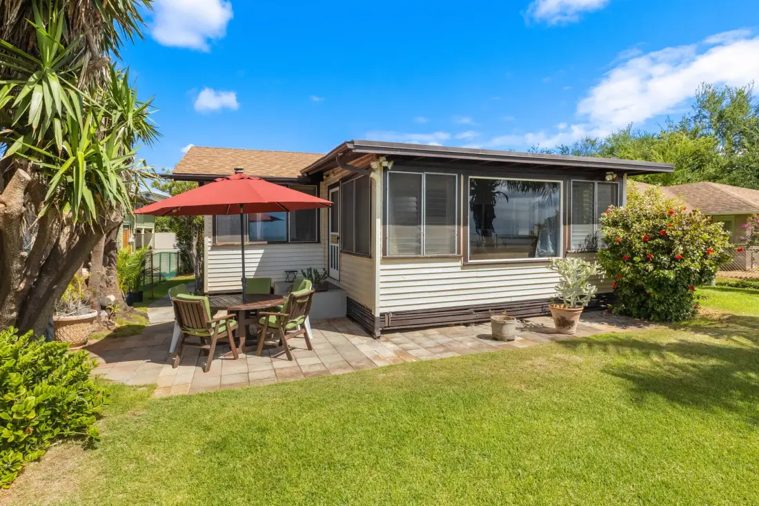 A single-story house with a patio table and red umbrella beside a green lawn.