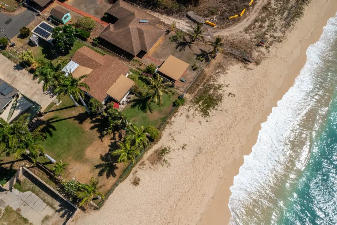 An aerial view of beachfront homes and palm trees beside a sandy shore.