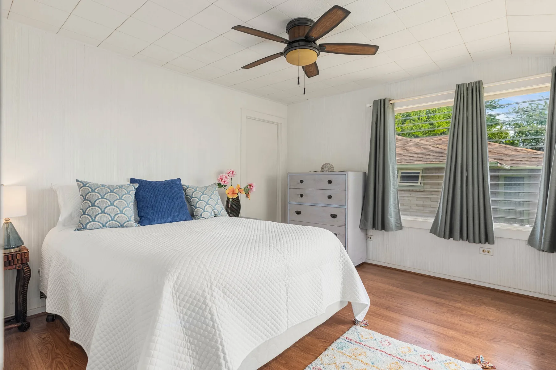 A bright bedroom with a neatly made bed and a window with curtains.