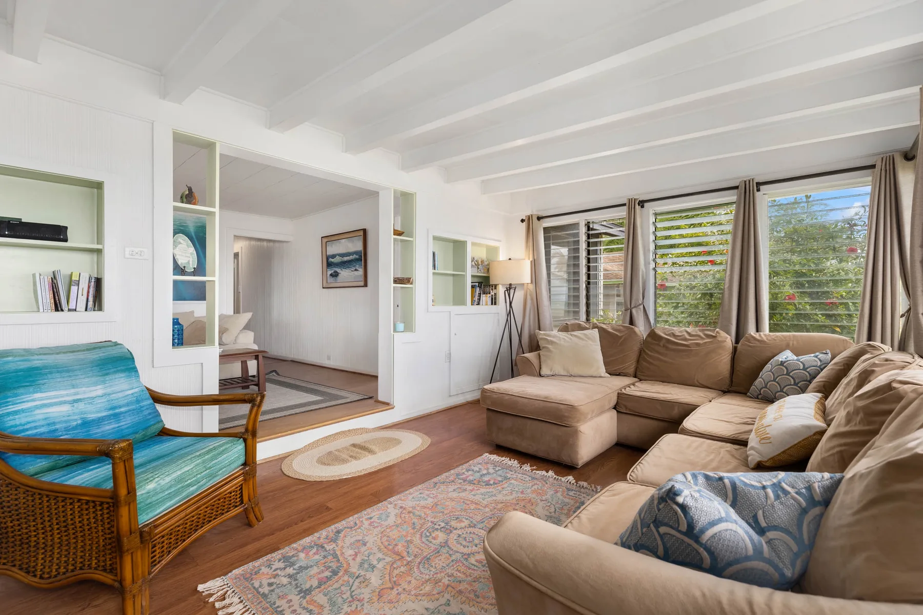 A bright living room with sectional seating, a woven armchair, and large windows.