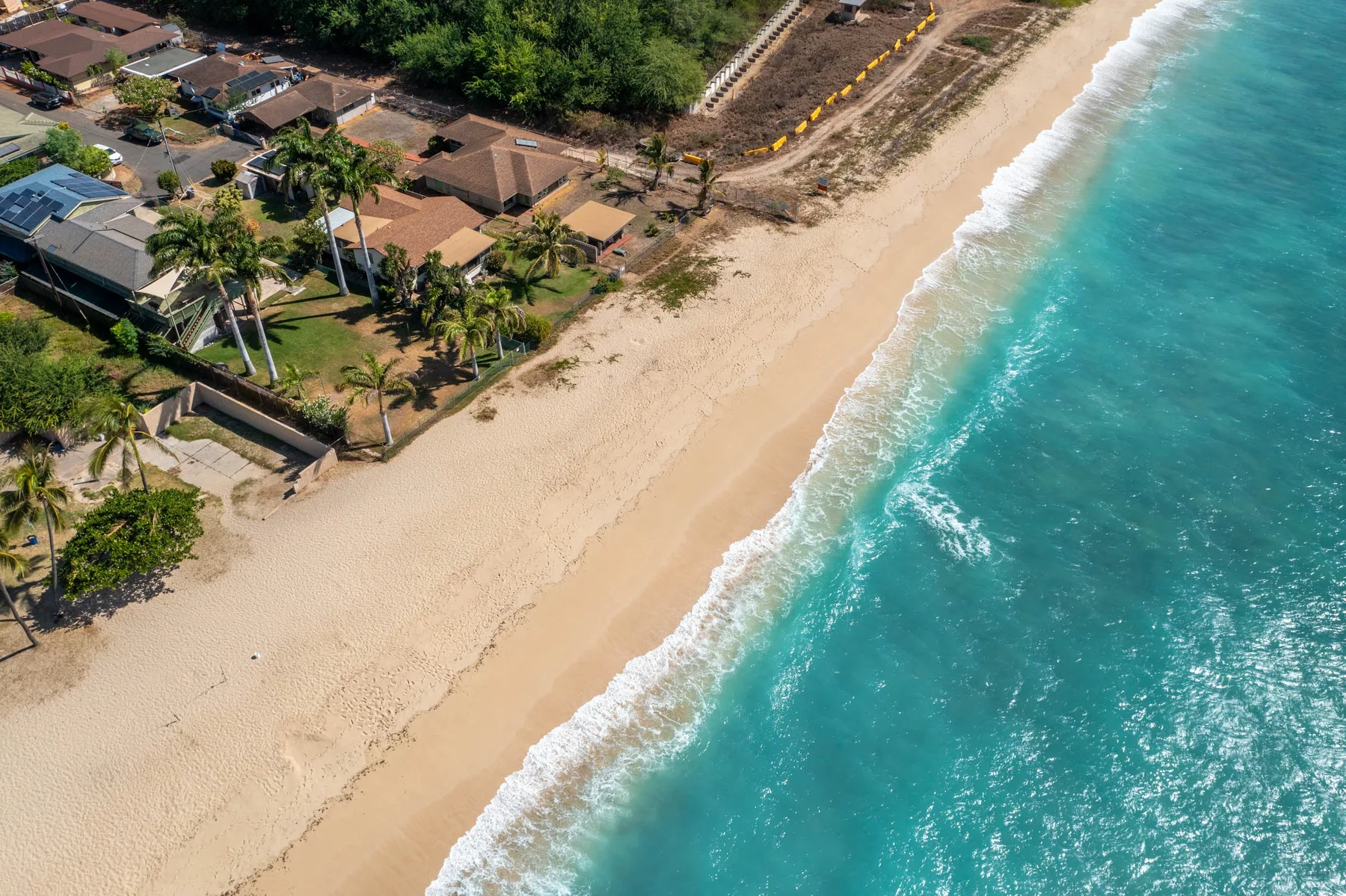 An aerial view of a sandy beach beside turquoise water and shoreline buildings.