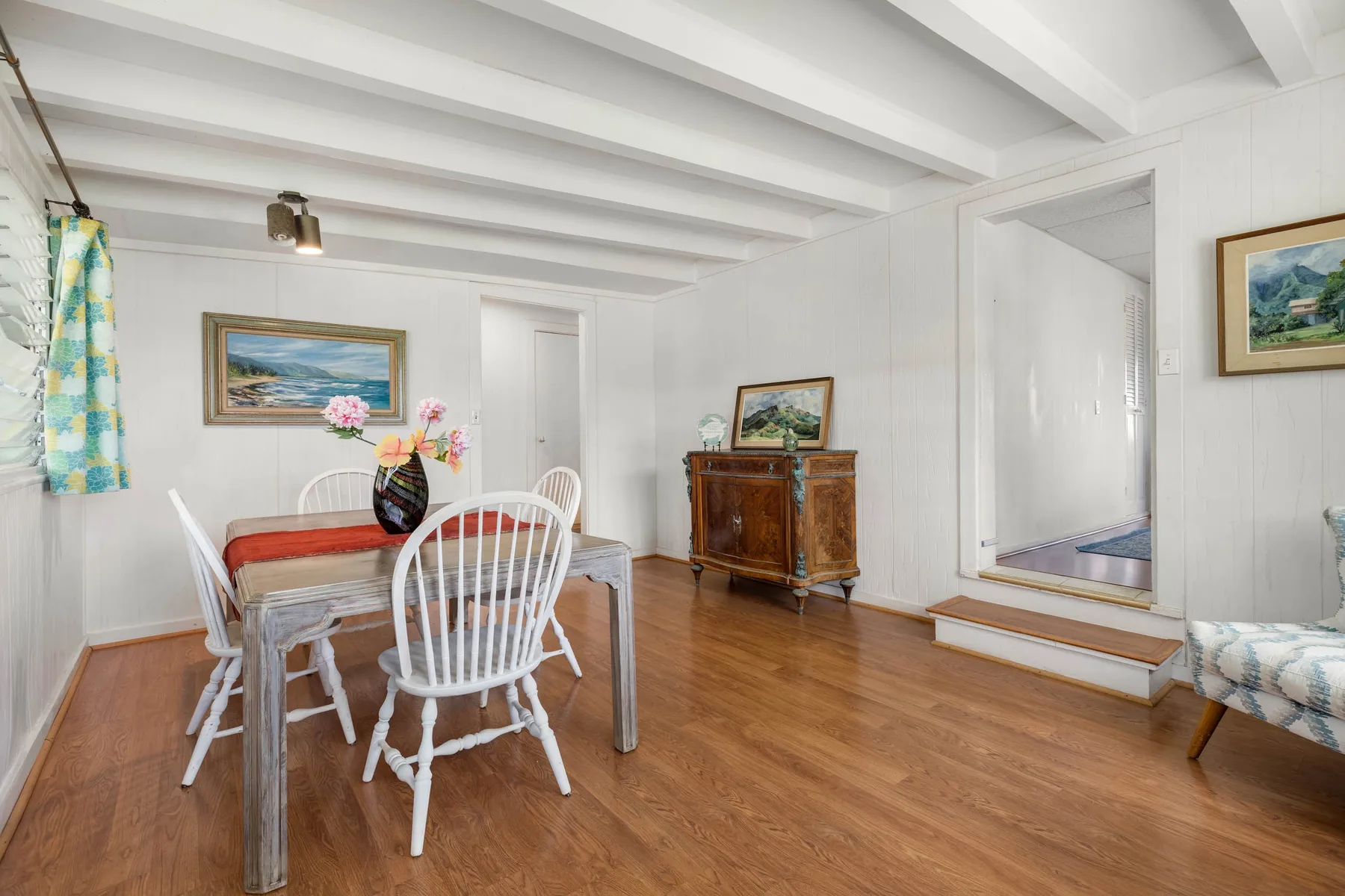 A bright dining area with a table, white chairs, and a wooden cabinet.
