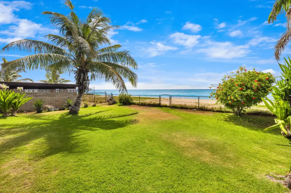 A sunny beachfront lawn with palm trees, flowering shrubs, and the ocean beyond.