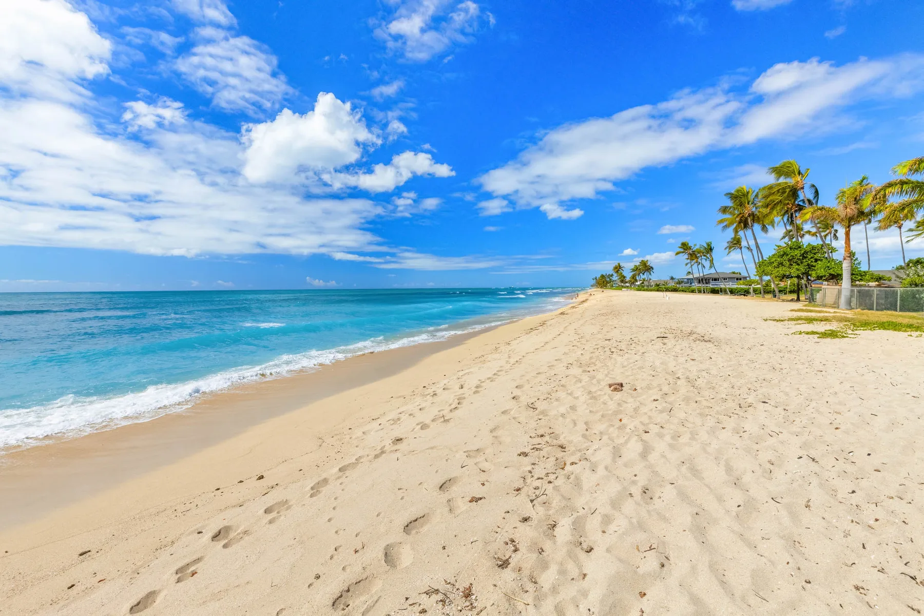 A sandy beach stretches beside turquoise water under a partly cloudy sky.