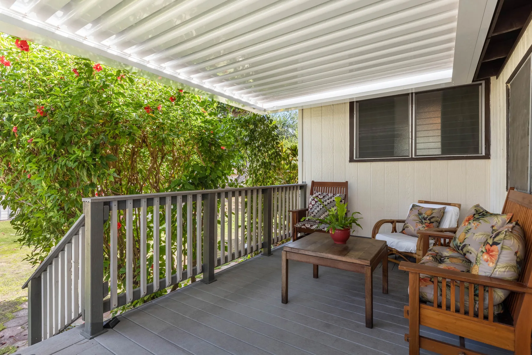 A covered patio has wooden seating and a table beside leafy plants.