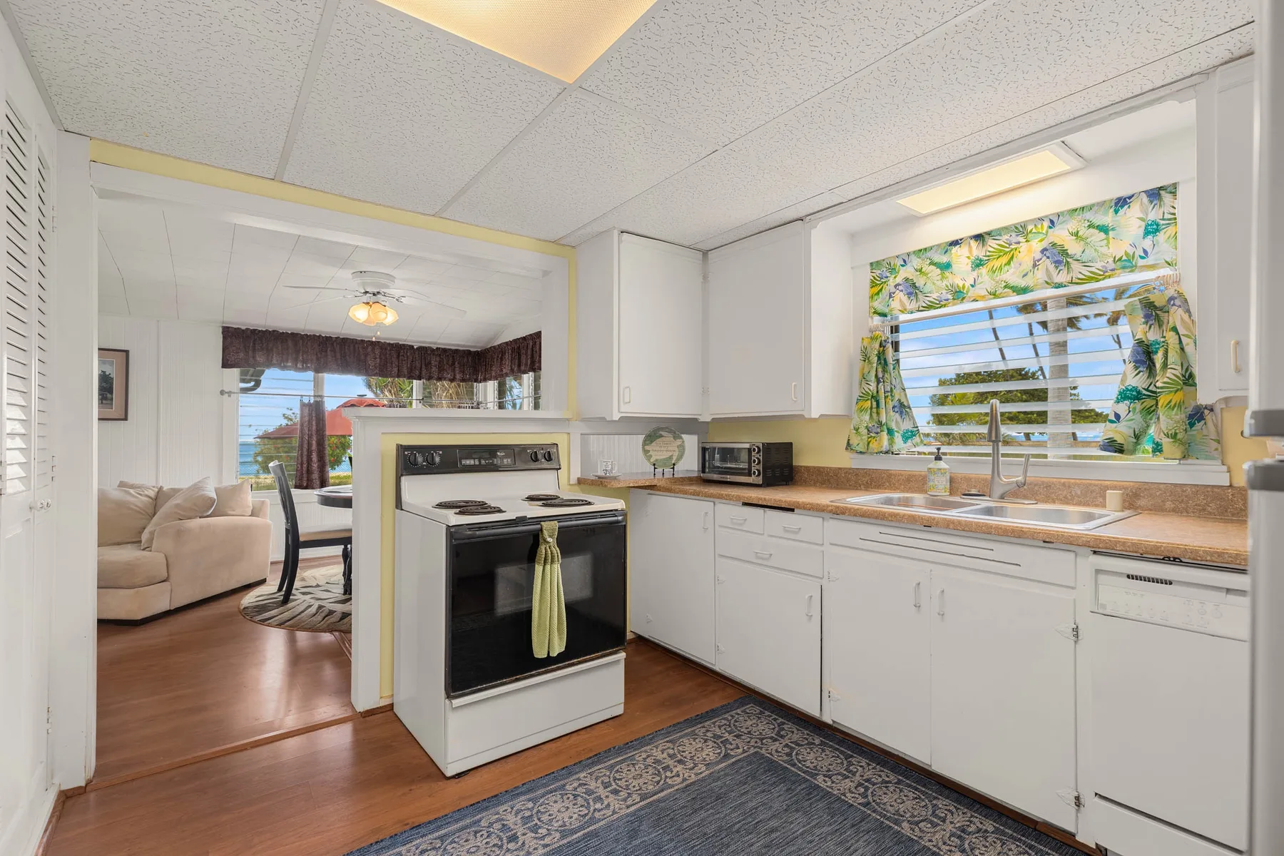 A kitchen with white cabinets and a stove opens into a living area.