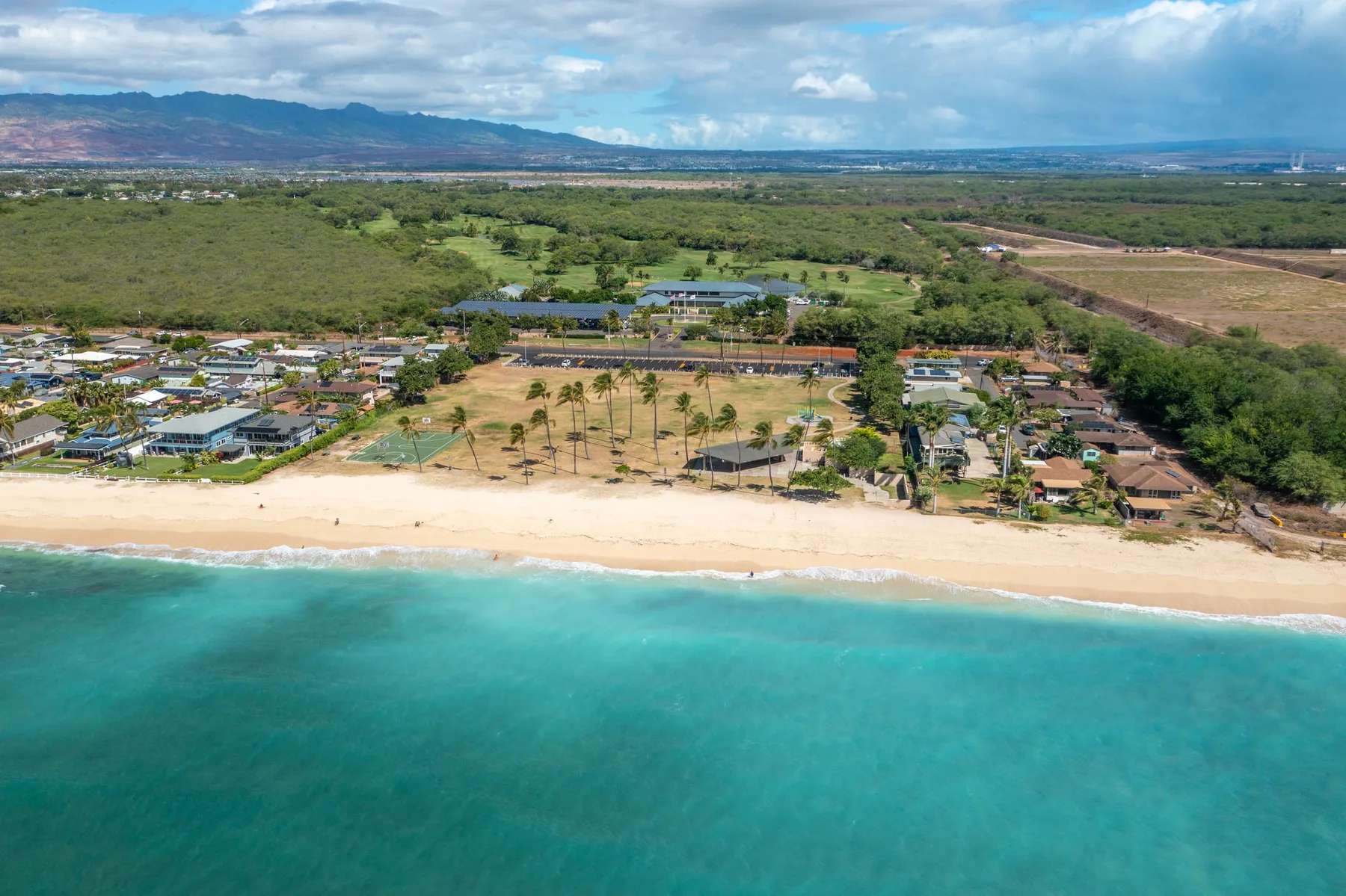 Aerial view of a sandy beach, turquoise water, and a green coastal landscape.