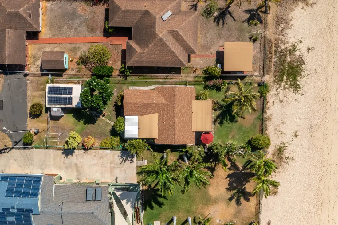 Aerial view of several buildings beside a sandy shoreline, with palm trees nearby.