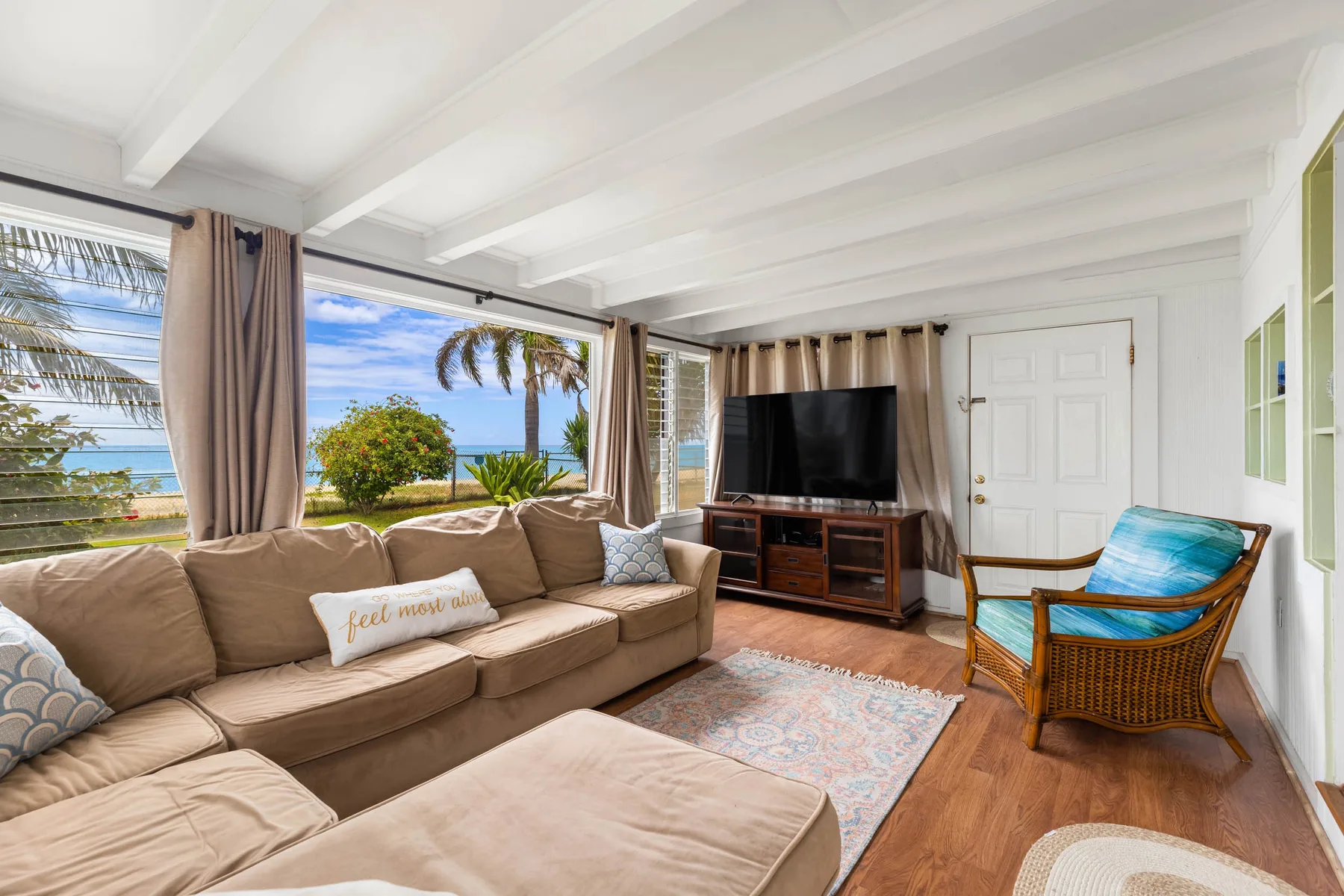 A bright living room with a sectional sofa, television, and ocean views through the windows.