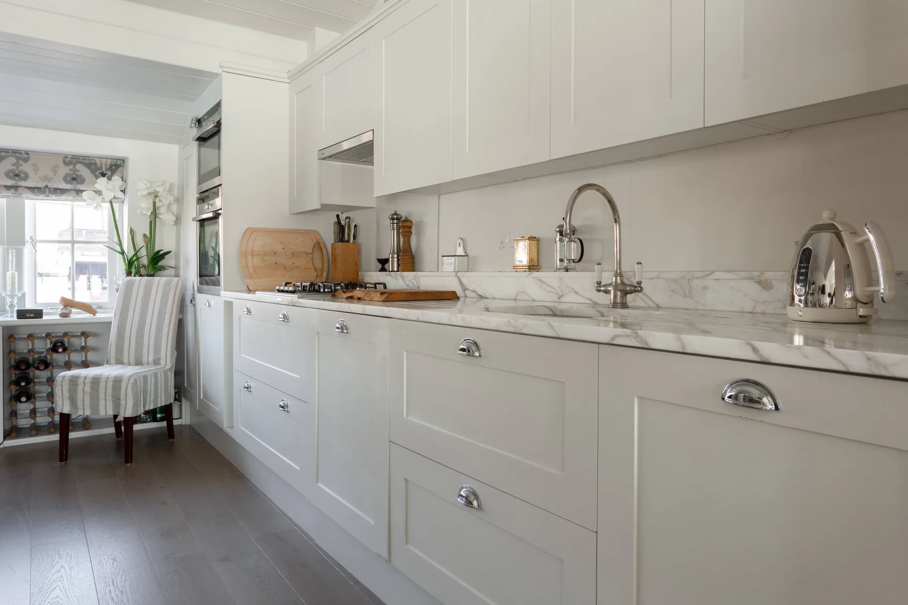 A bright kitchen with white cabinetry, a marble countertop, and a dining area by the window.