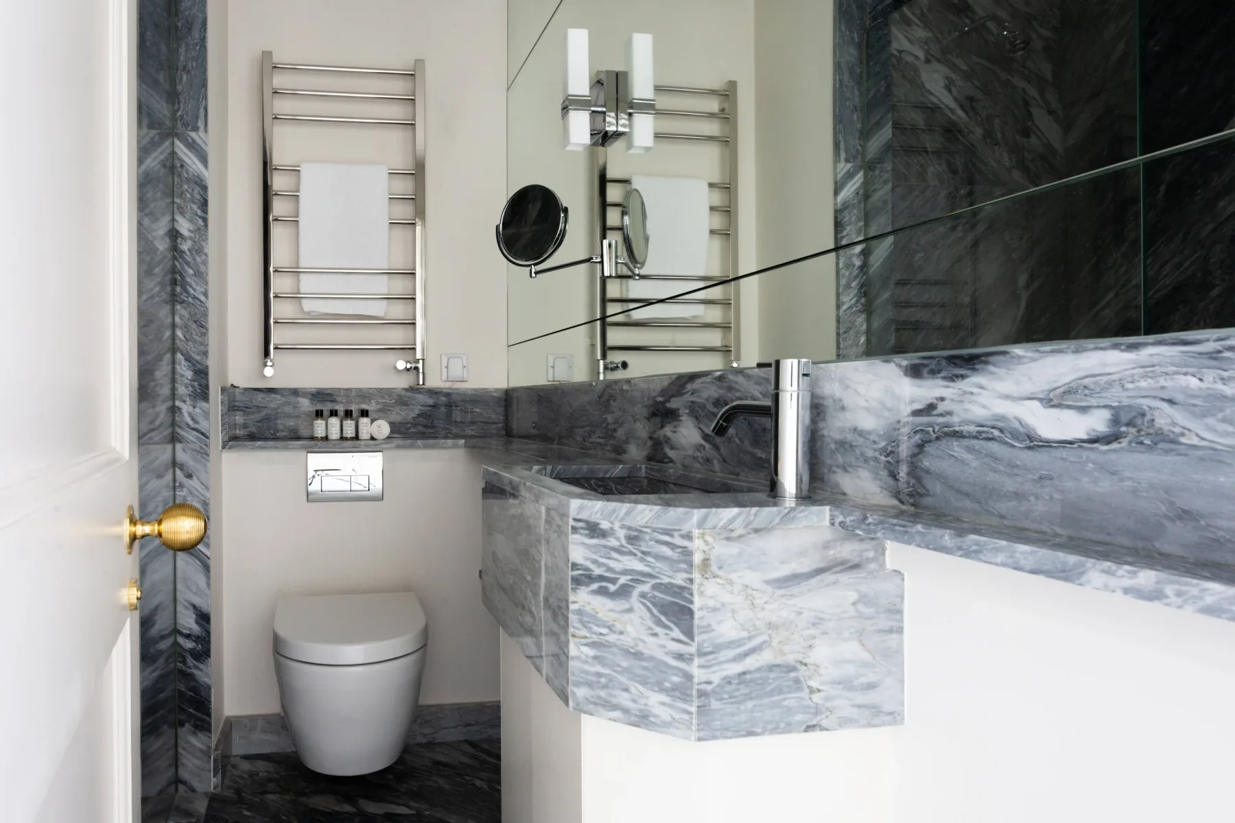 A modern bathroom with a toilet, wall-mounted towel warmer, and marble vanity.