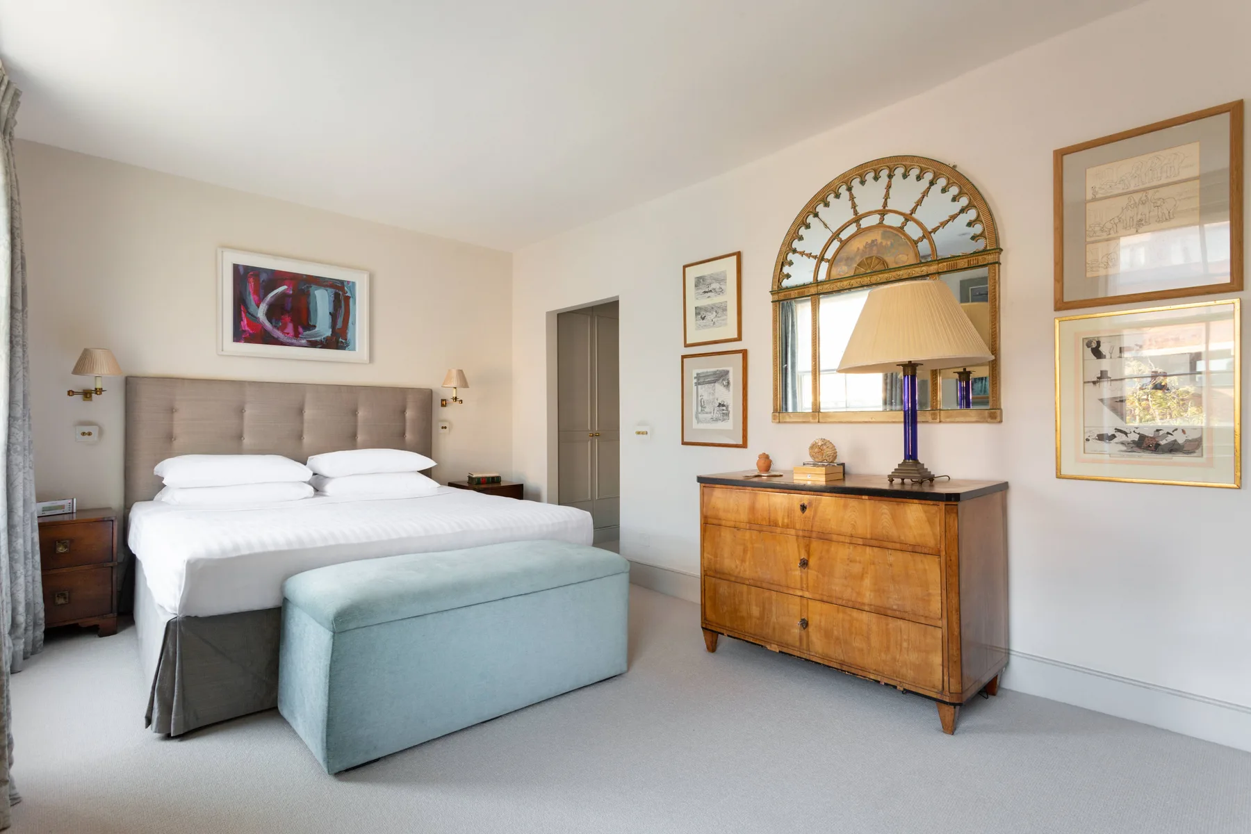 A bedroom with a large bed and a wooden dresser beneath a mirror.
