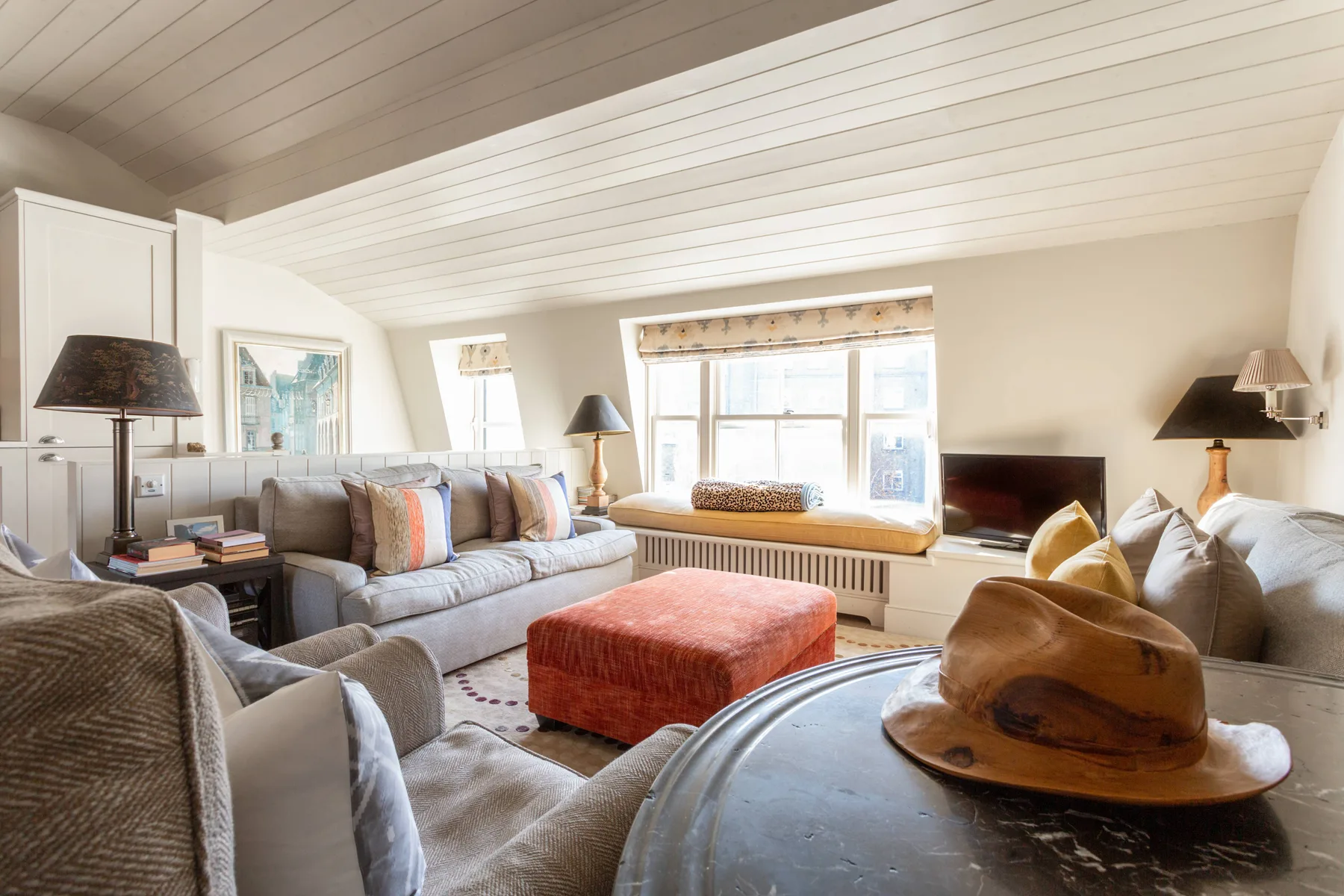 A bright living room with seating arranged around a window and ottoman.