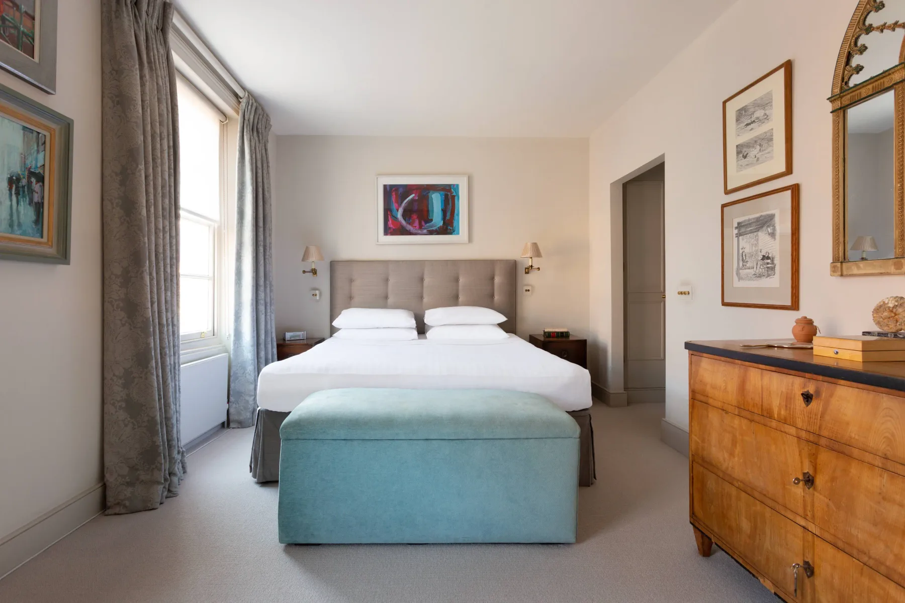 A bedroom with a neatly made bed and a teal upholstered bench at its foot.