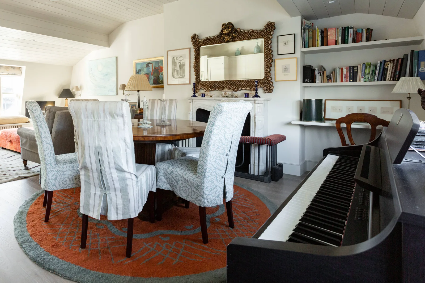 A dining area with a round table and chairs beside a piano and built-in bookshelves.