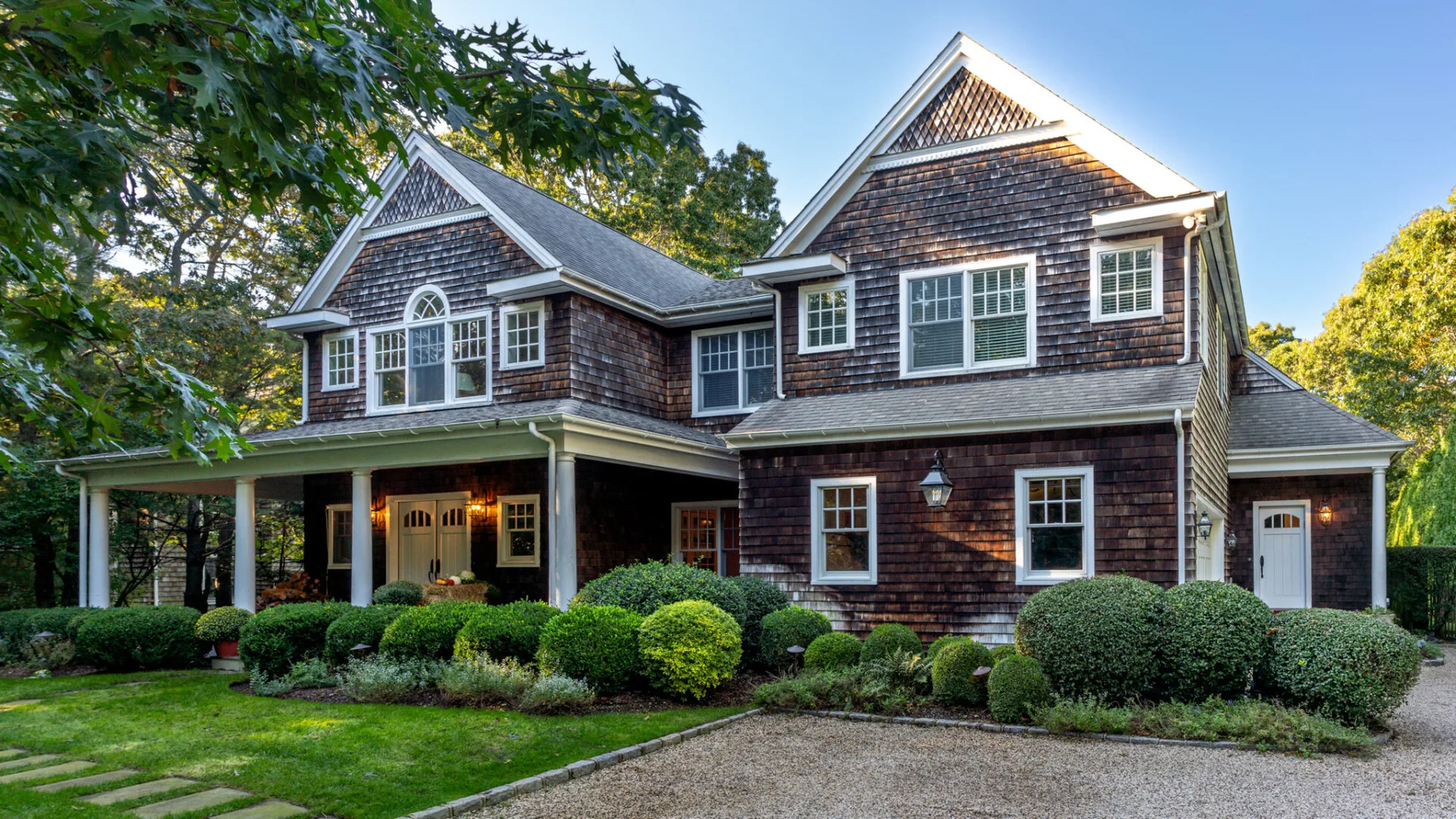 A large house with dark shingle siding, white trim, and a landscaped front yard.