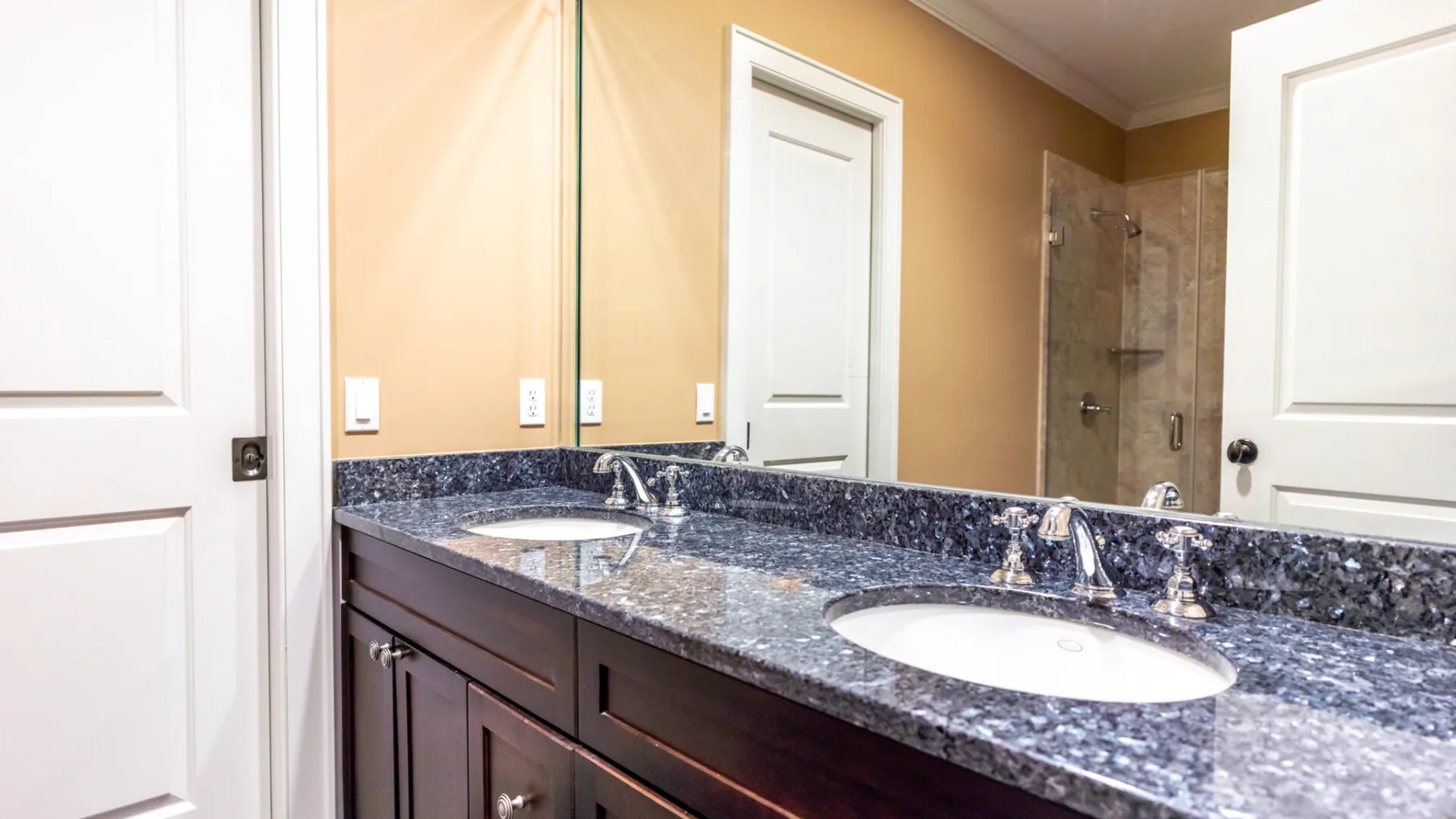 A bathroom vanity with two sinks and a mirror faces a glass shower.