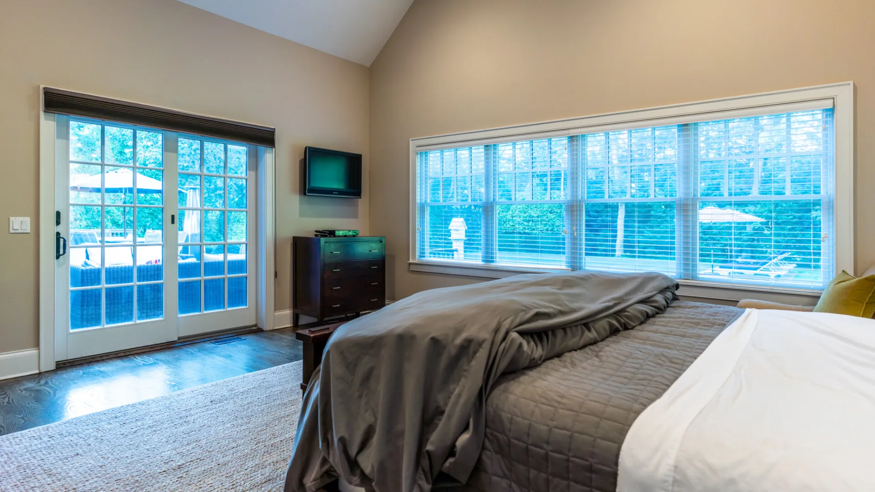 A bedroom with a large bed beside broad windows and a glass door.
