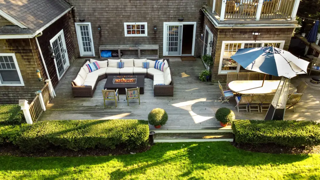 An outdoor deck with lounge seating and a dining table beneath an umbrella.