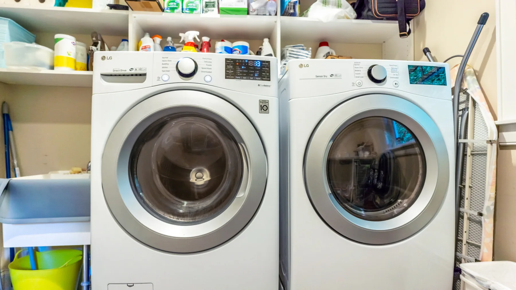 A laundry room with a front-loading washer and dryer beneath shelves.