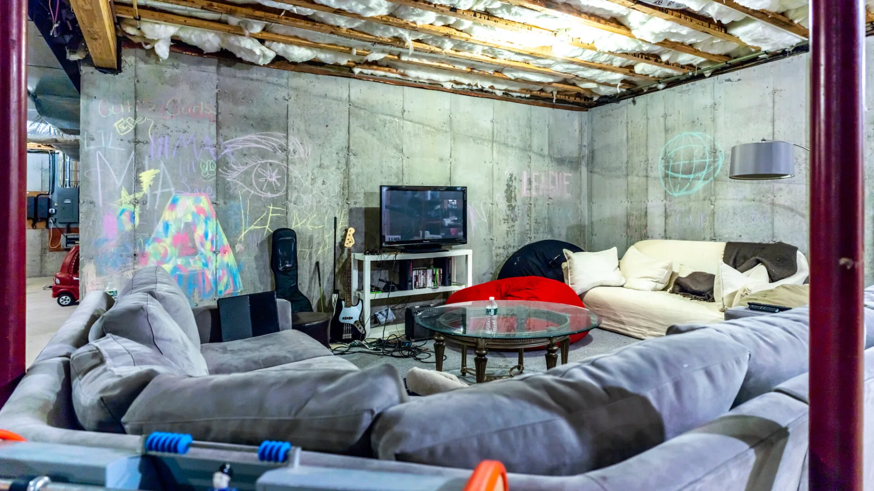 A lounge with gray seating, a television, and colorful graffiti on concrete walls.