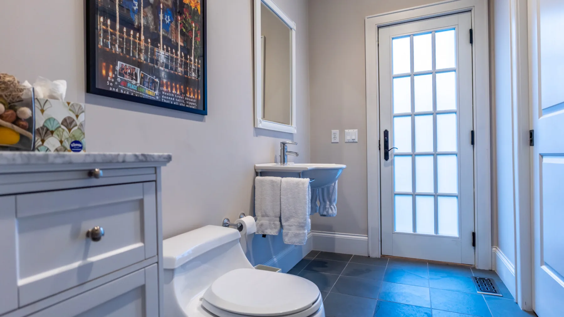 A bathroom with a vanity, toilet, and glass-paneled door.