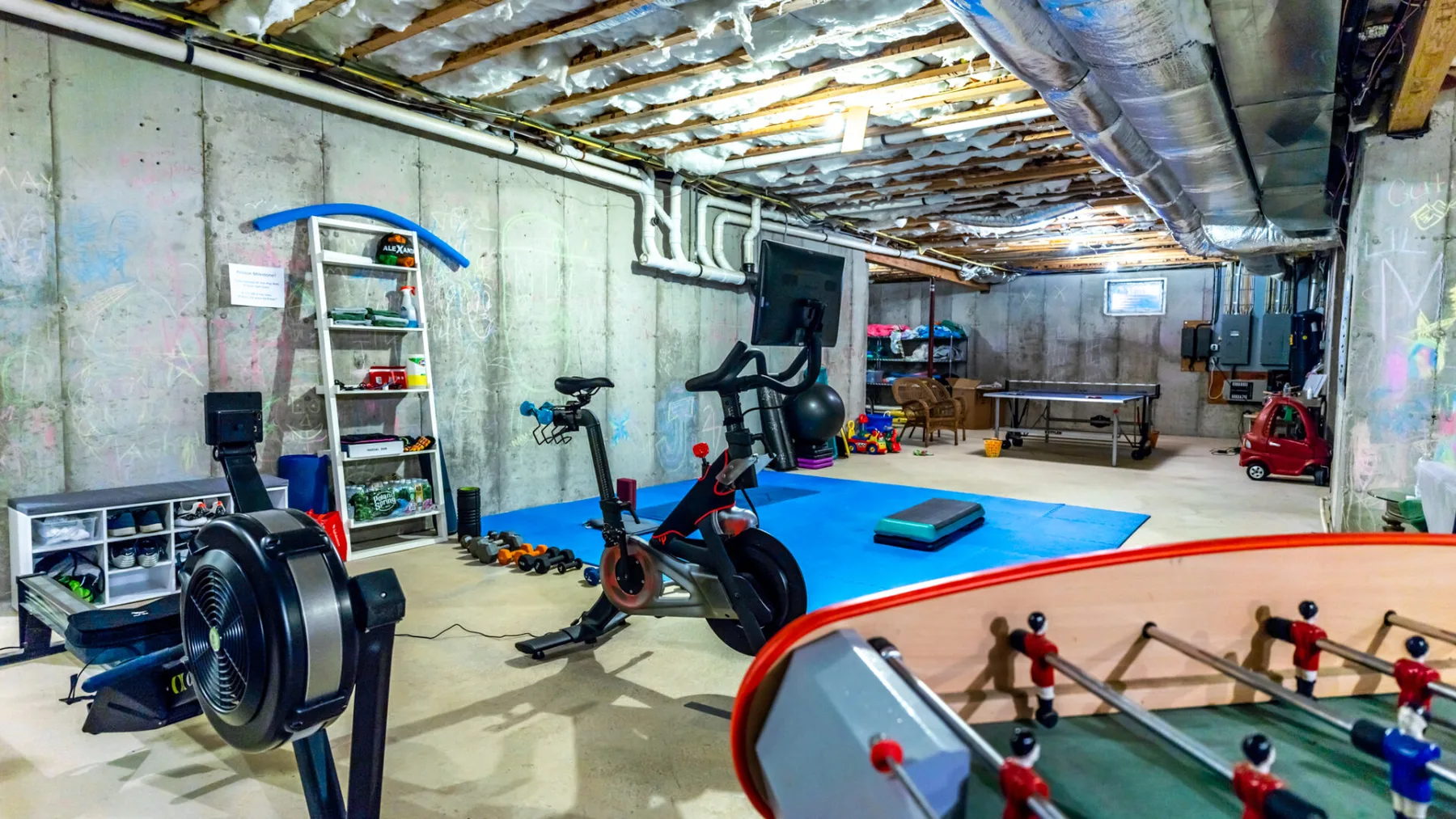 A basement recreation room with exercise equipment, a mat, and a foosball table.