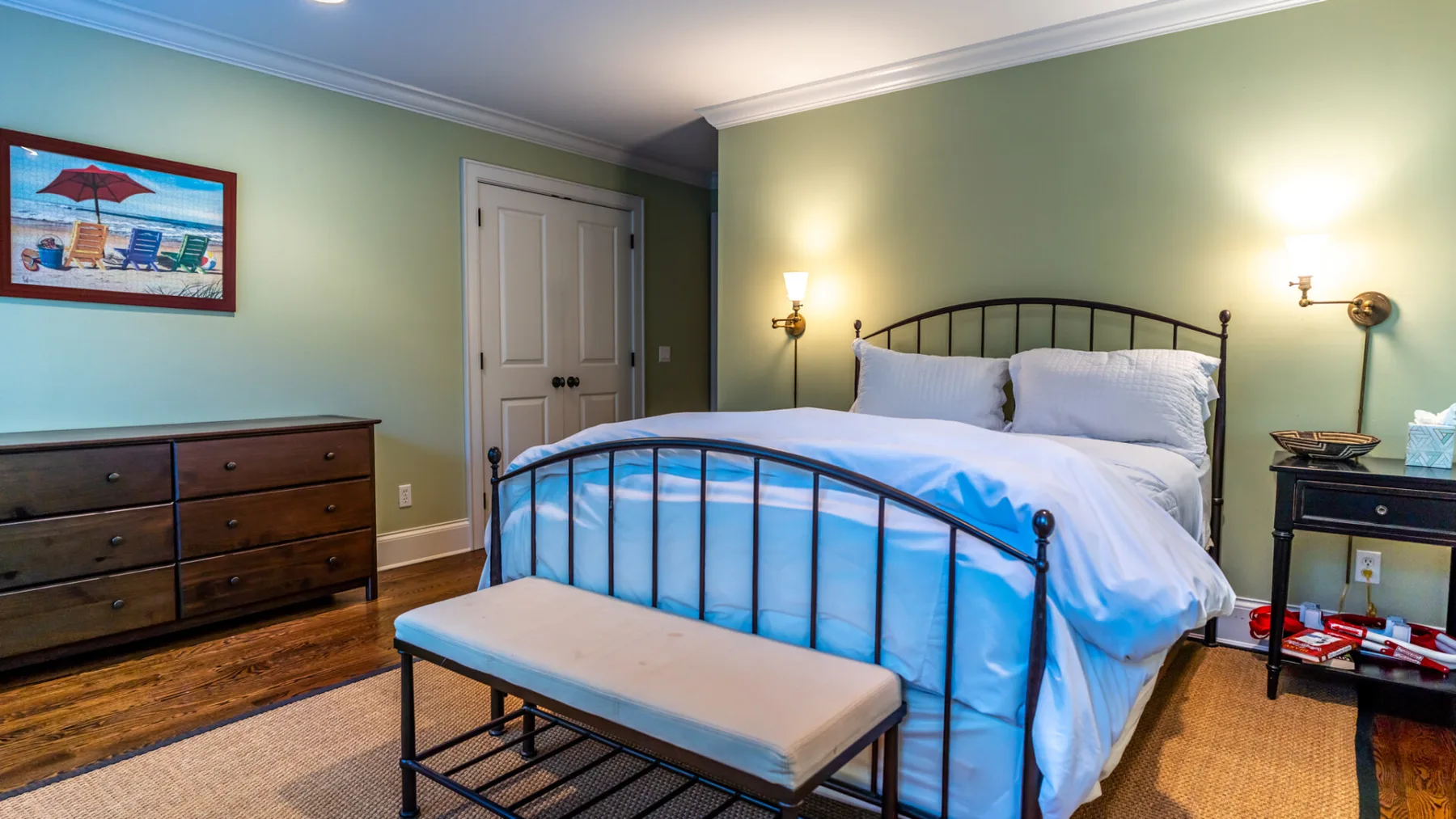 A bedroom with a bed, bench, and dresser against pale green walls.