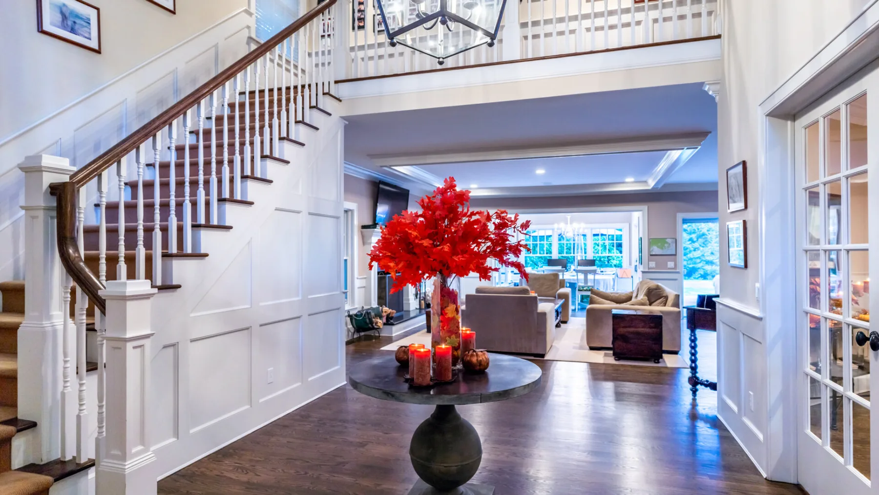 A bright foyer with a staircase, a round table, and a red floral arrangement.