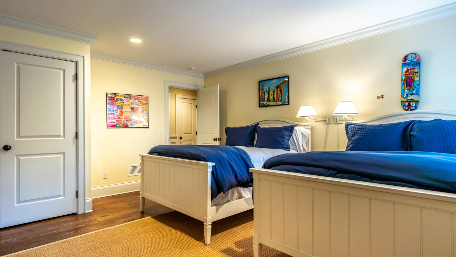 A bedroom with two beds, blue bedding, and light-colored paneled bed frames.