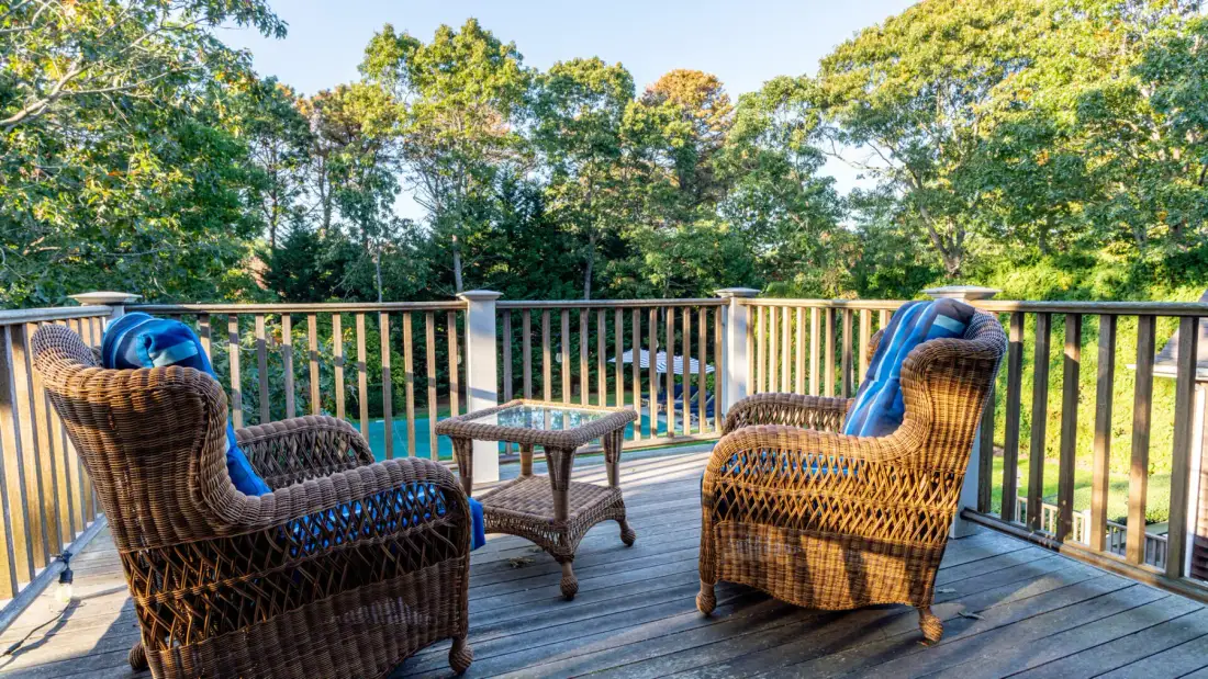 A wooden deck with wicker seating overlooks a tree-lined outdoor area.