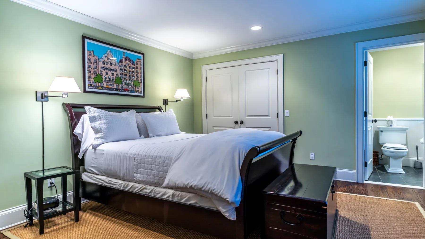 A bedroom with a neatly made bed and an open doorway to a bathroom.