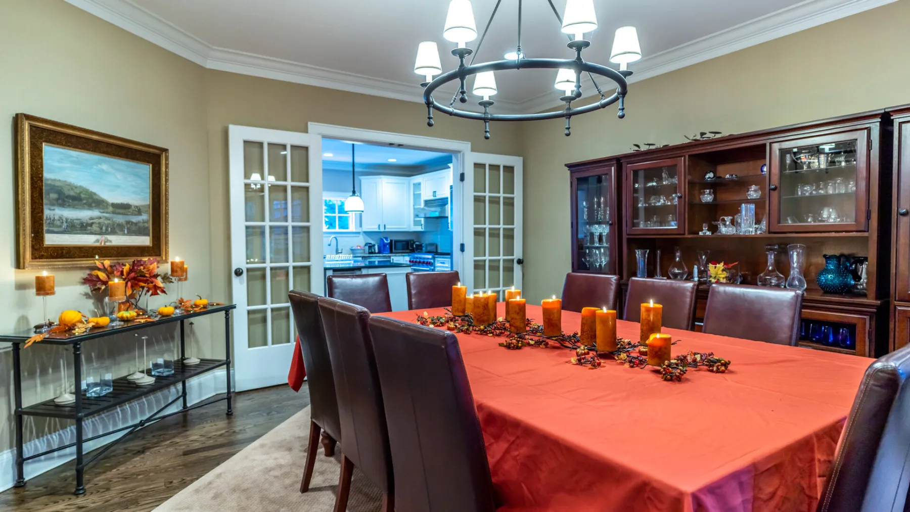 A dining room with a large table covered in a red tablecloth and a wooden display cabinet.