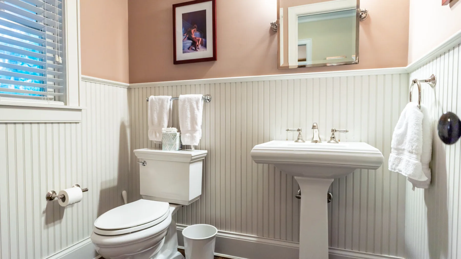 A bathroom with a pedestal sink and toilet beneath a wall mirror.