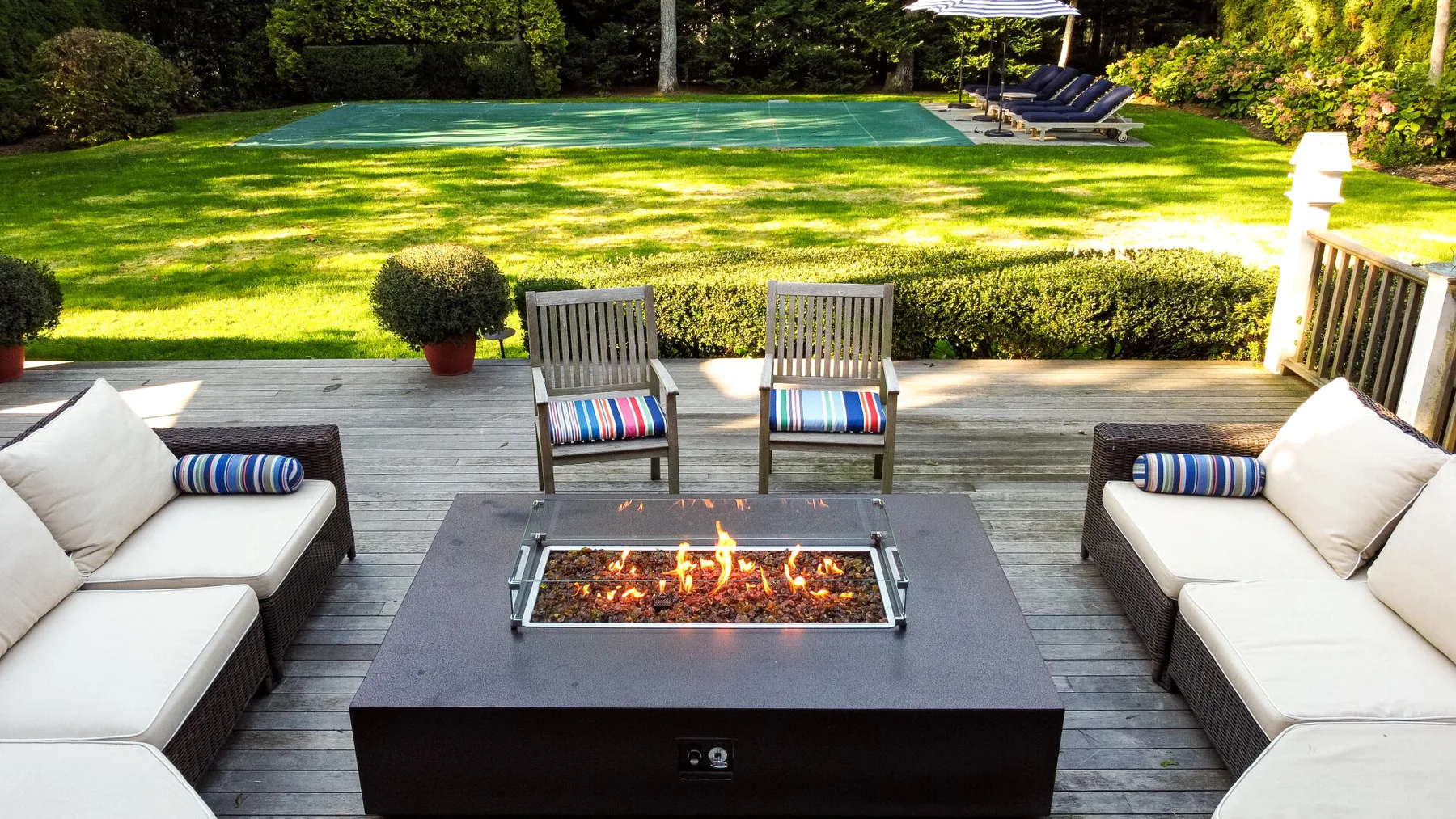 An outdoor seating area surrounds a lit fire pit beside a lawn and swimming pool.