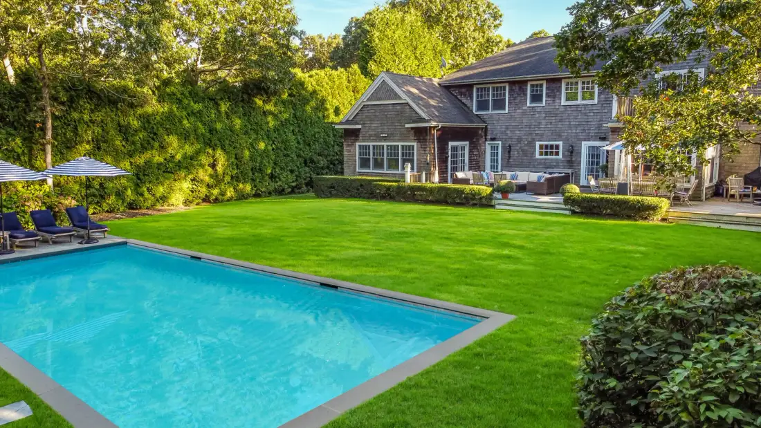 A landscaped backyard with a swimming pool and a large house.