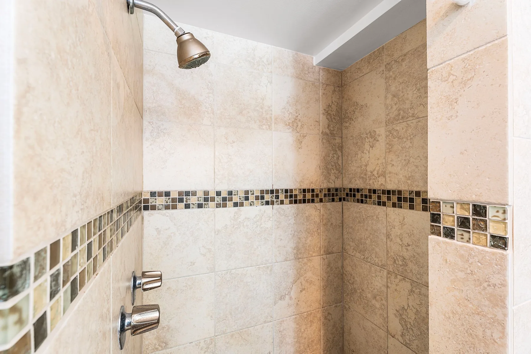 Una ducha con paredes de azulejos y una franja decorativa de mosaico.